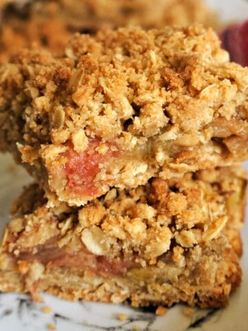 2 slices of rhubarb crumble bars piled up on a white plate.