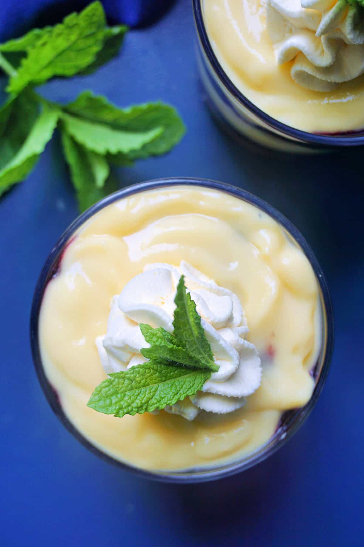 Overhead of a glass with trifle, fresh mint leaves on the side and a partially visible glass at the top.