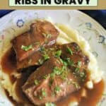A plate with a portion of mash topped with beef chunks in gravy and garnished with chopped parsley.