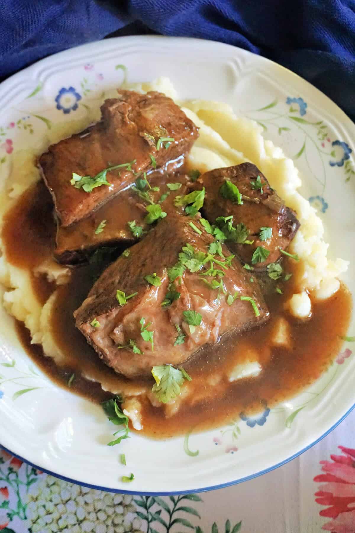 A plate with beef chunks in gravy garnished with chopped parsley and served over a bed of mash.