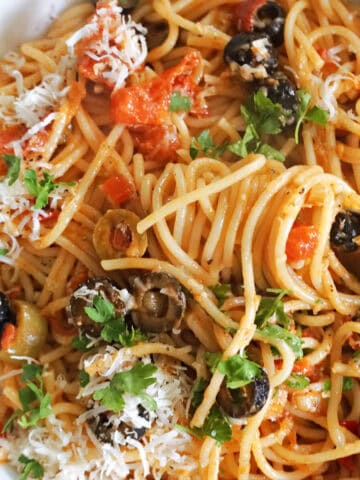 A portion of spaghetti puttanesca with a fork twirling the spaghetti.