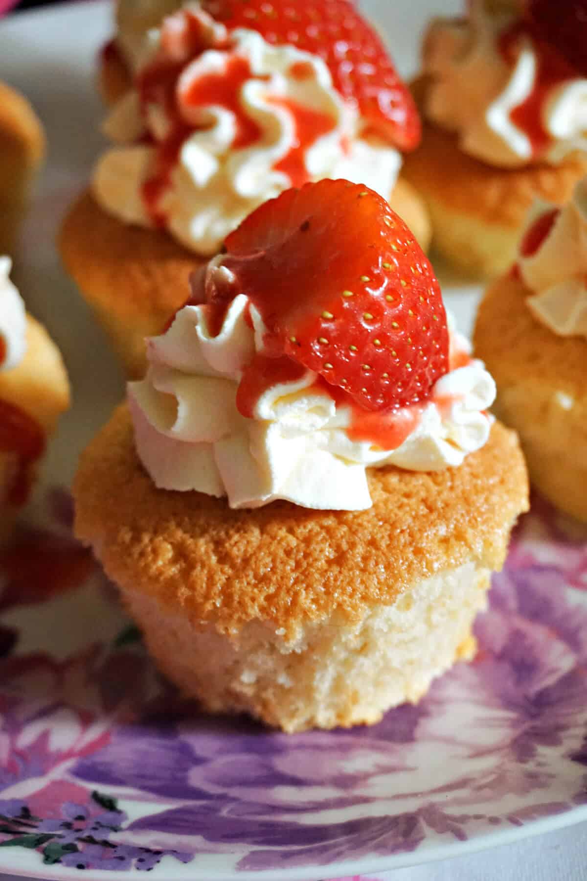 A cupcake topped with cream, strawberry sauce and half a strawberry.