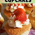 A cupcake topped with cream, strawberry coulis and fresh strawberry slices. Other partially-visible cupcakes around.