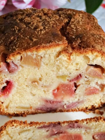 A white plate with a sliced fruit loaf and a partially visible slice of cake.