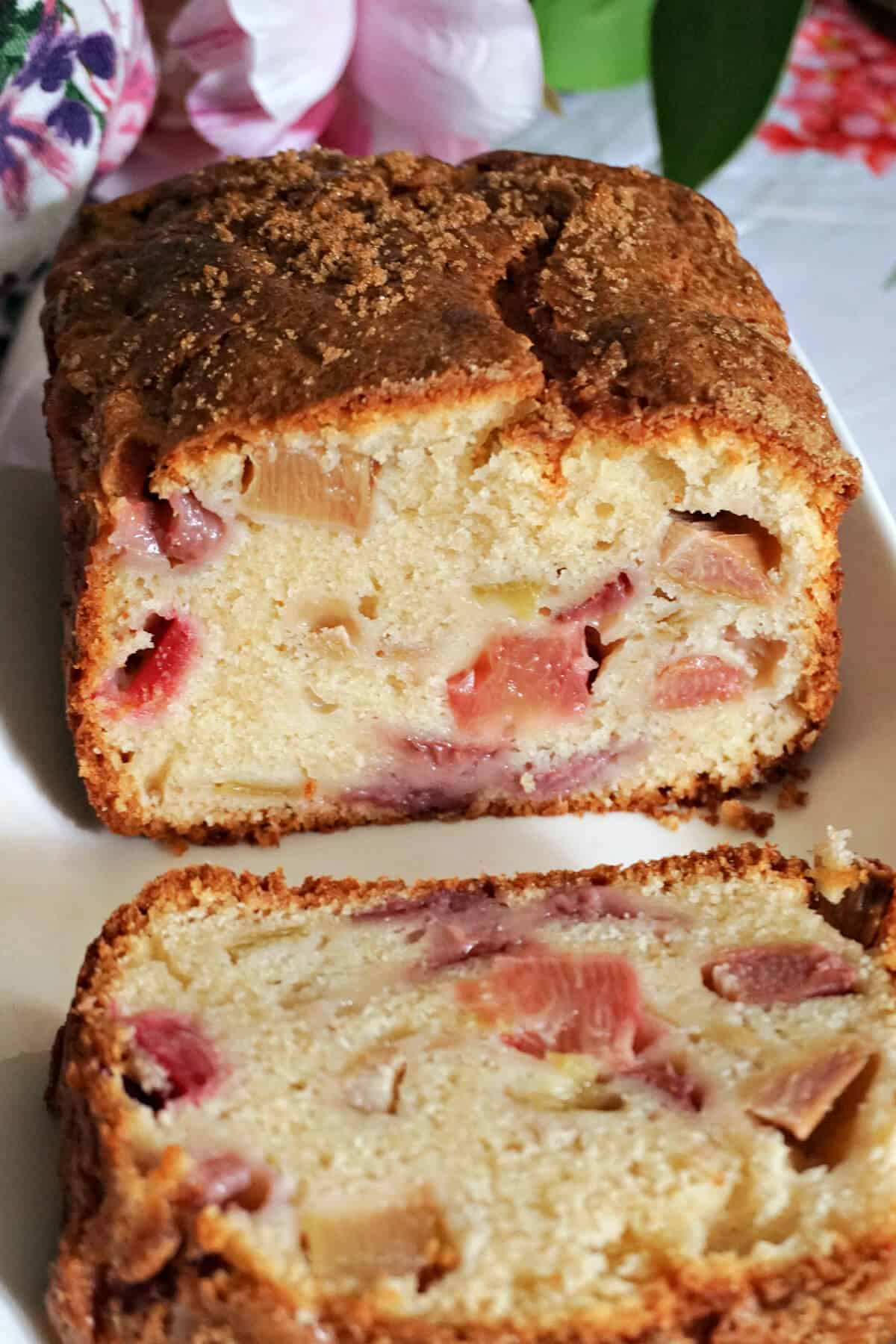 A white rectangle plate with a sliced loaf cake with flowers blurred in the background.