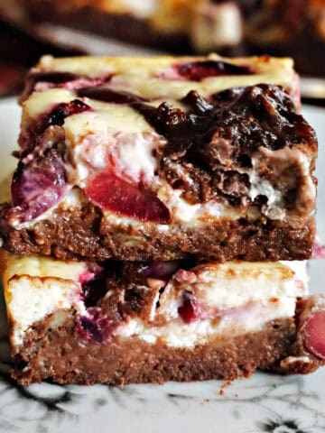A stack of 2 cheesecake brownie bars on a white plate.