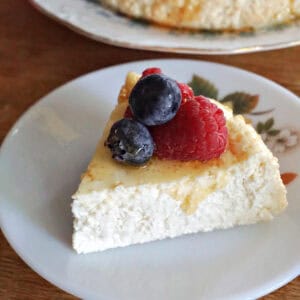 A slice of crustless cheesecake topped with berries and honey on a small dessert plate.