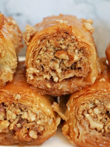 A white plate with 3 baklava rolls and other 2 partially visible rolls.