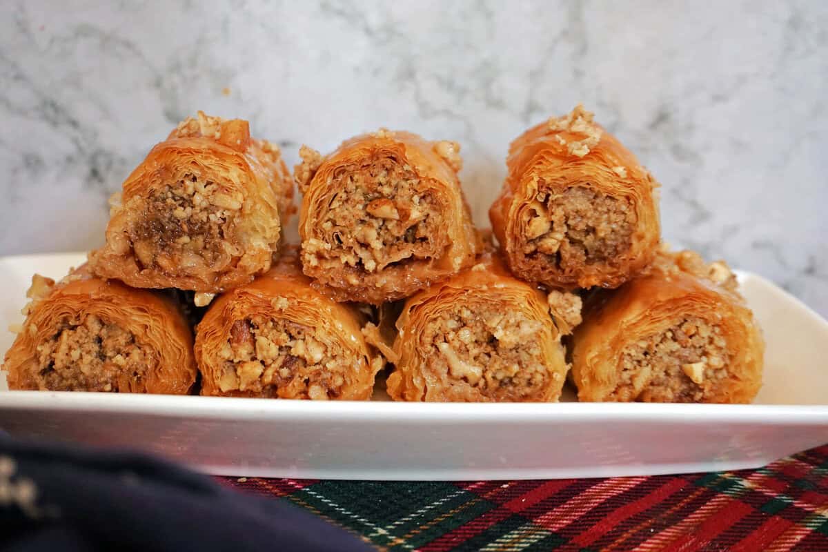 A white rectangle plate with 7 baklava rolls.