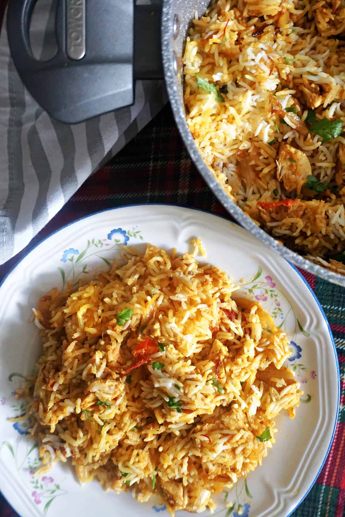 A white plate with a portion of chicken biryani and a partially-visible pot with biryani.