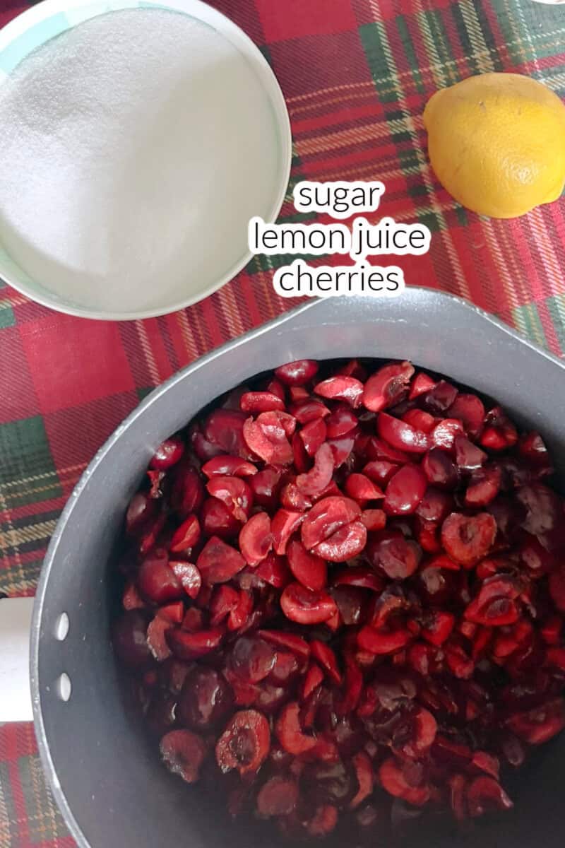 A pot with chopped cherries, a small bowl with sugar and a lemon on a tabletop.