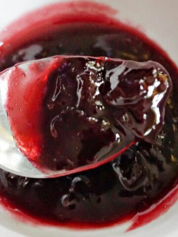 A spoonful of jam over a white ramekin with jam.