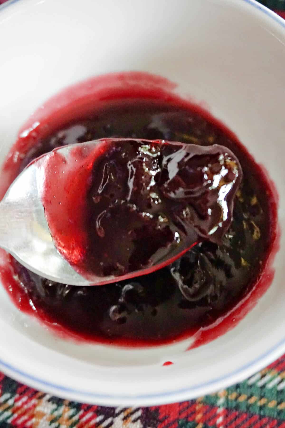 A spoonful of cherry jam over a small bowl with jam.