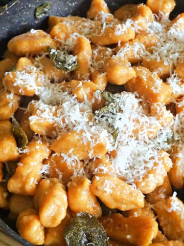 A pan with sweet potato gnocchi topped with grated parmesan cheese.