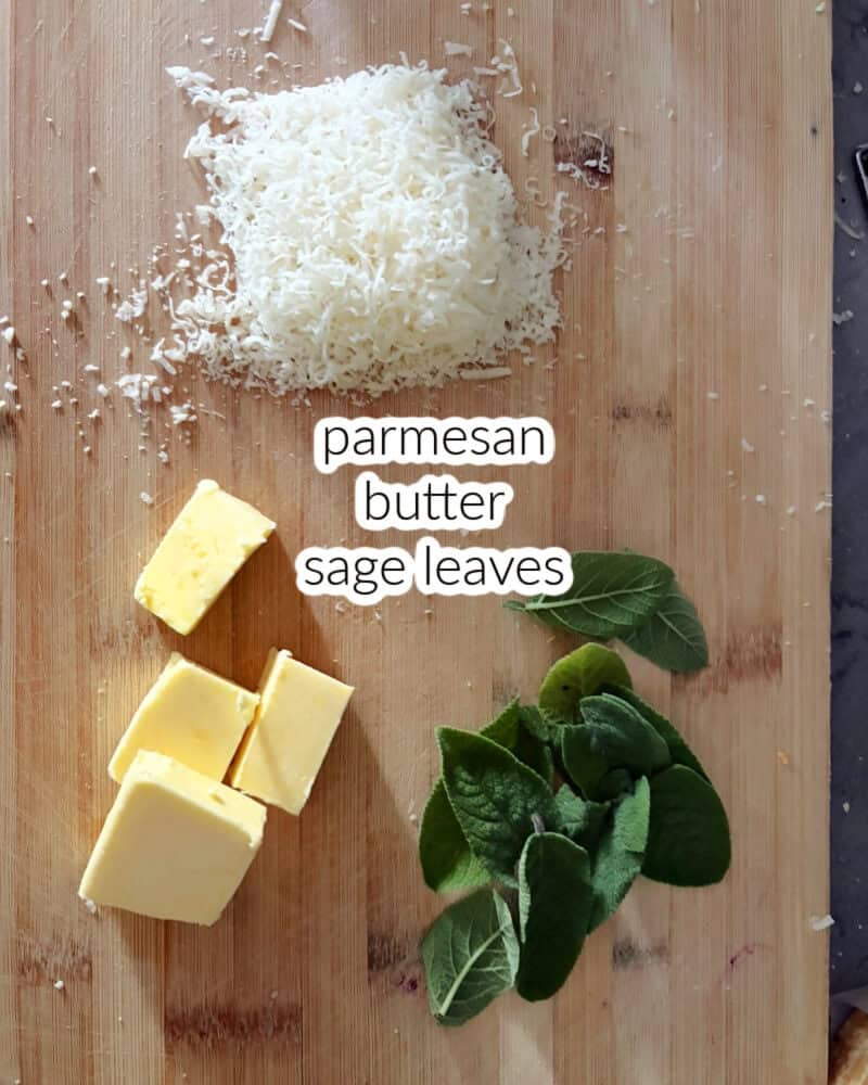 A wooden board with grated cheese, fresh sage leaves and 4 cubes of butter.