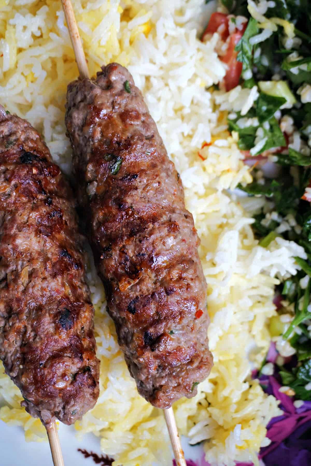 2 kofta kebabs over a bed of yellow rice with salad on the side.