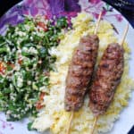 A flowery plate with 2 kofta kebab skewers on a bed of saffron rice and salad.