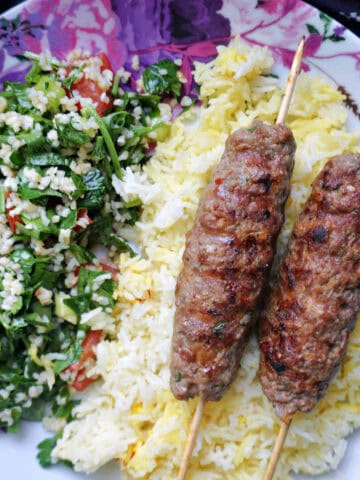 A flowery plate with 2 kofta kebab skewers on a bed of saffron rice and salad.