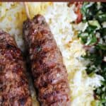 Close-up of 2 kotfata kebab skewers on a bed of gold rice and salad.