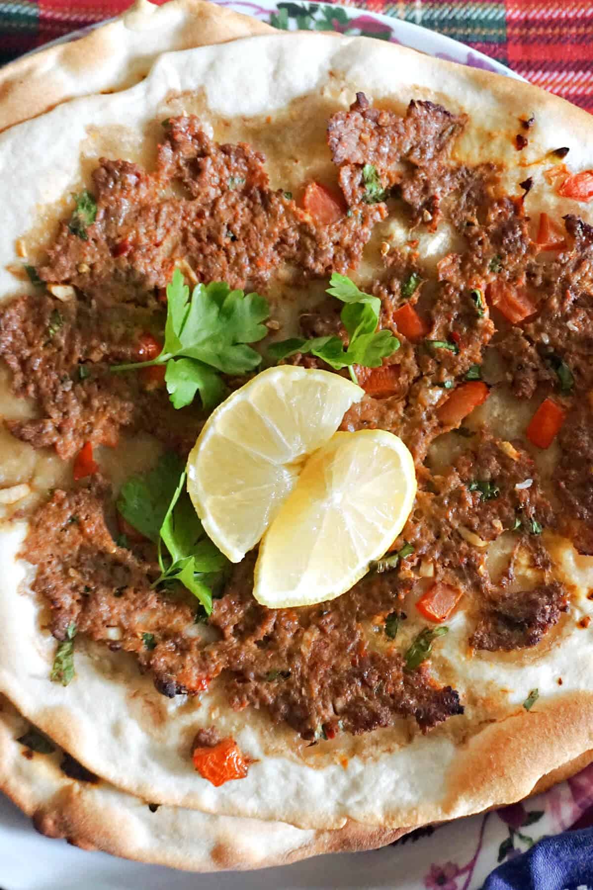 Close-up of a Turkish pizza garnished with 2 lemon wedges and fresh parsley leaves.