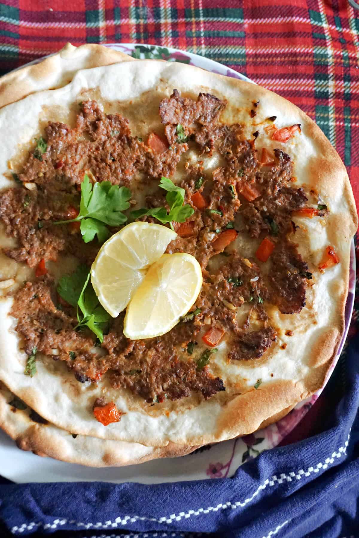 A flatbread topped with mince and garnished with 2 lemon wedges and fresh parsley.