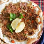 A flatbread topped with mince and garnished with 2 lemon wedges and fresh parsley.