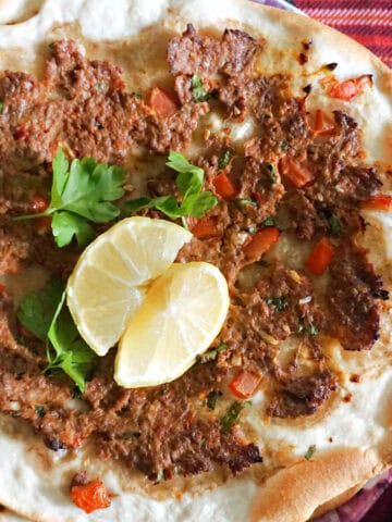 A flatbread topped with mince and garnished with 2 lemon wedges and fresh parsley.