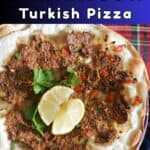 A pile of flatbreads topped with mince and garnished with lemon wedges and fresh parsley.