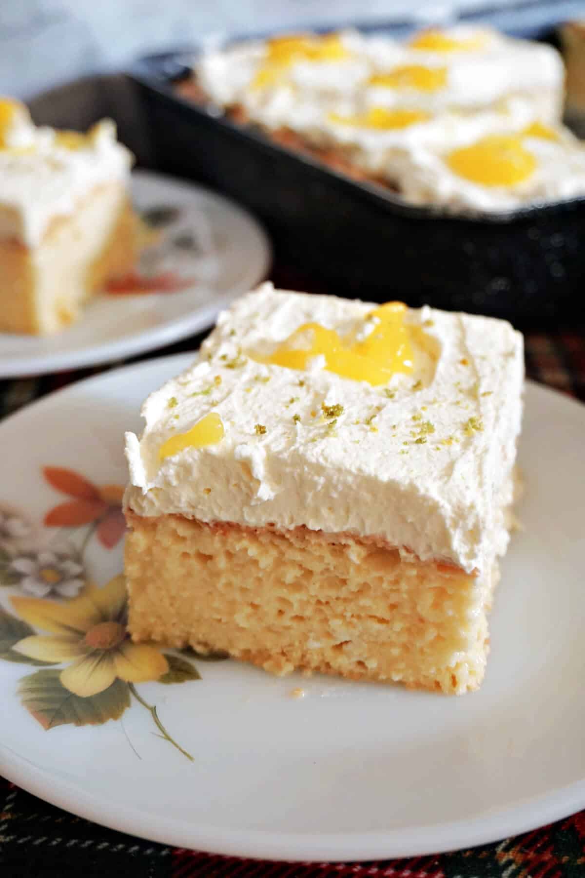 A slice of tres leches cake on a white flowery plate.