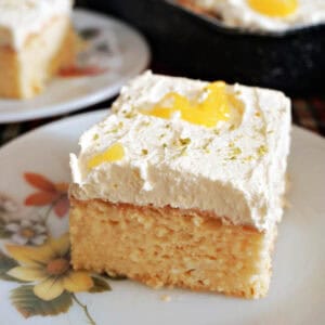 A white flowery dessert plate with a slice of sponge cake decorated with cream and lemon curd.