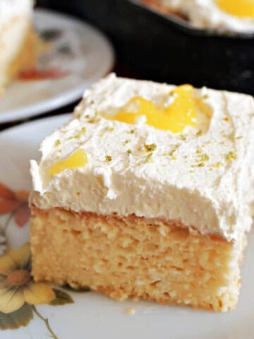A white flowery dessert plate with a slice of sponge cake decorated with cream and lemon curd.