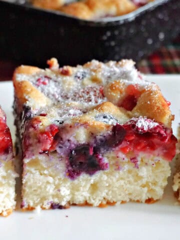 A slice of berry cake on a white plate with partially-visible slices of cake next to it.