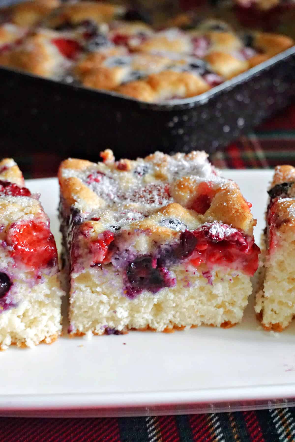 Close-up of a white rectangle plate with 3 partially-visible berry cake slices and a cake tray at the top.