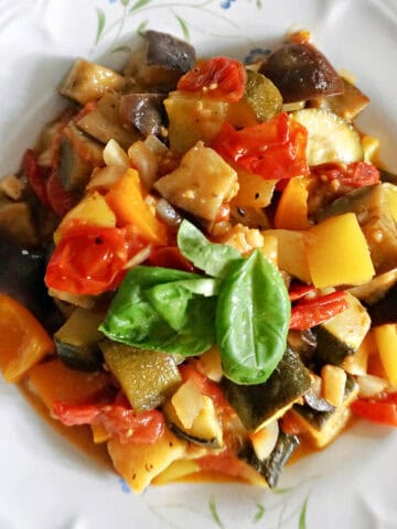A plate with a portion of veggie stew garnished with fresh basil leaves.