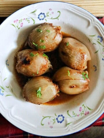 A white flowery plate with stuffed onions in broth.