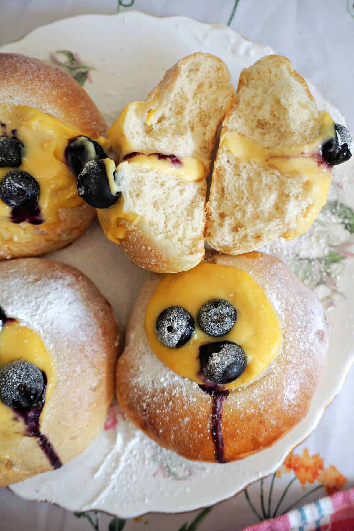 2 halves of a brioche surrounded by 3 whole brioche topped with custard and blueberries.