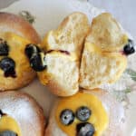 A white plate with 2 halves of a custard and blueberry bun and 3 other partially-visible buns.