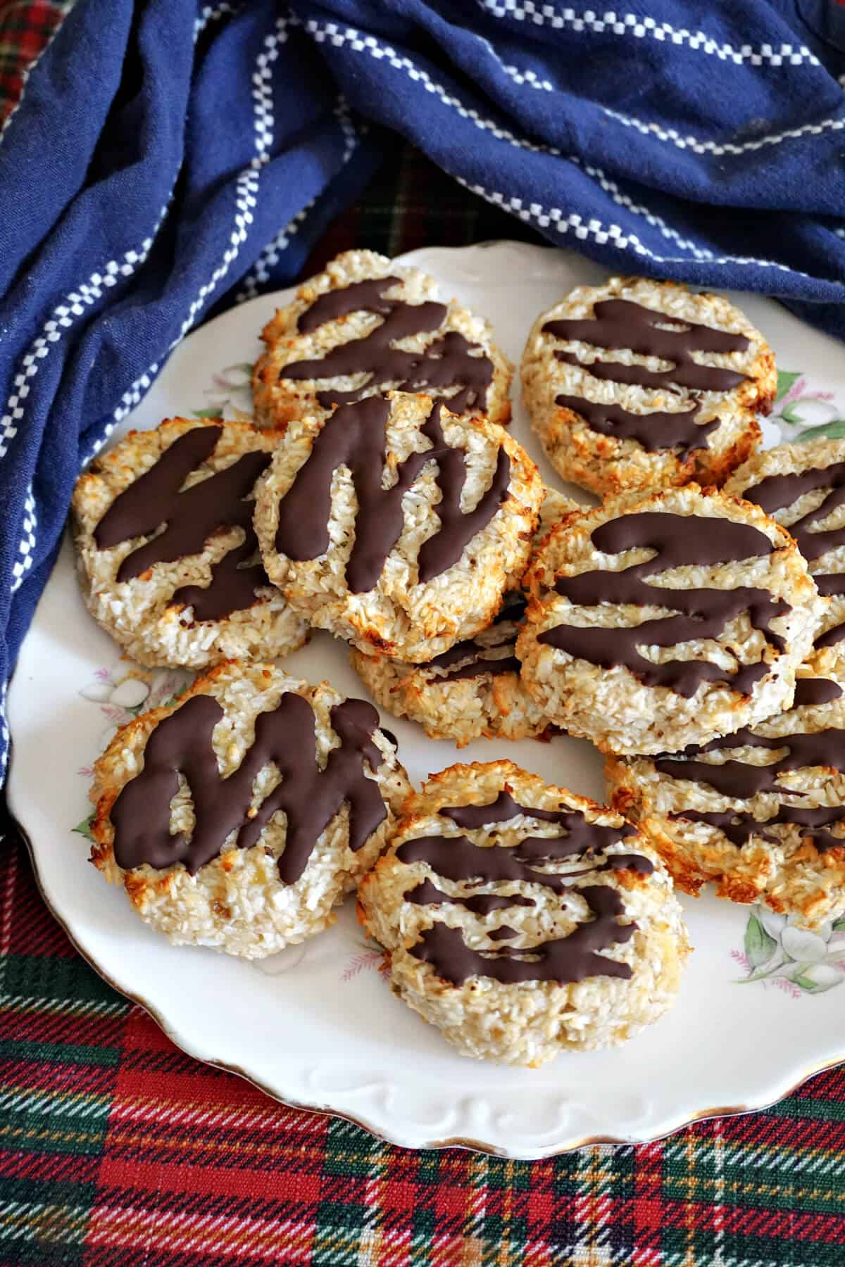 A plate with coconut cookies drizzled with dark chocolate and a blue kitchen towel around the plate.