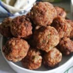 A pile of meatballs on a white serving bowll with a kitchen towel around the bowl.