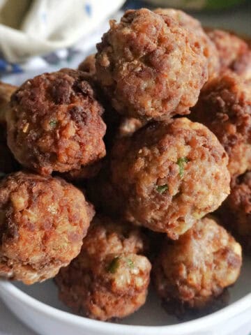 A pile of meatballs on a white serving bowll with a kitchen towel around the bowl.