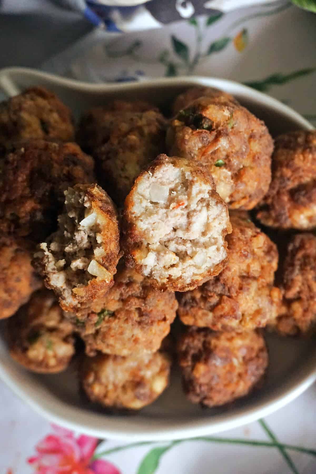 A white bowl with meatballs, and 2 half meatballs sitting on top of a pile of meatballs.
