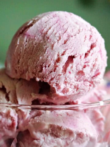 A dessert glass with scoops of blackberry ice cream. A green blackground.