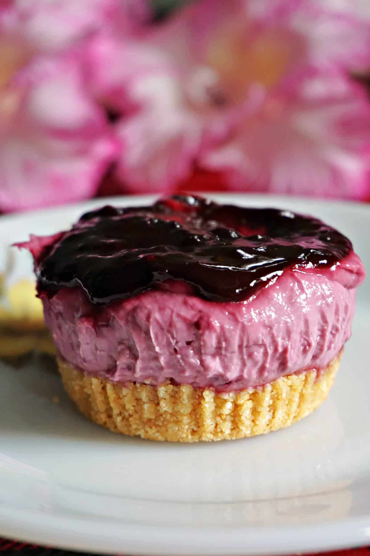 A white plate with a mini blackberry cheesecake.