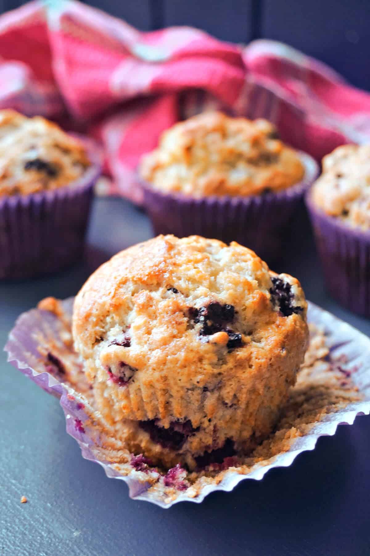 A blackberry muffin on a muffin case with other muffins partially-visible in the background.