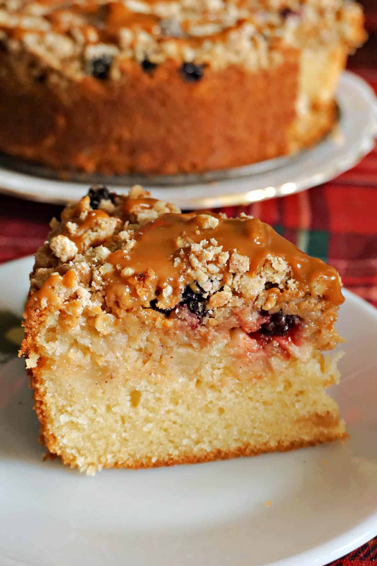 A slice of cake on a white plate with the rest of the cake in the background.