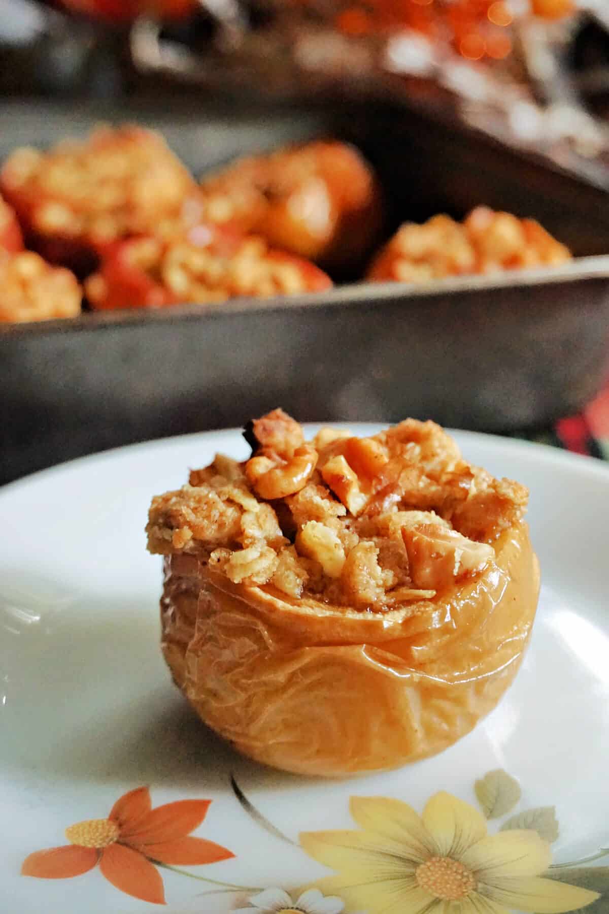 A stuffed apple on a small plate with a tray of stuffed apples blurry in the background.
