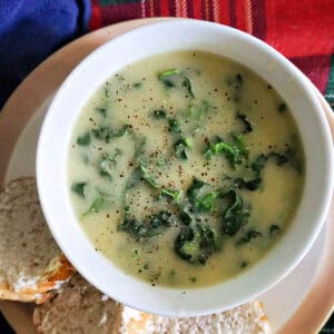 A white bowl with creamy soup on a white plate with 3 slices of baguette.
