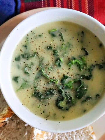 A white bowl with creamy soup on a white plate with 3 slices of baguette.