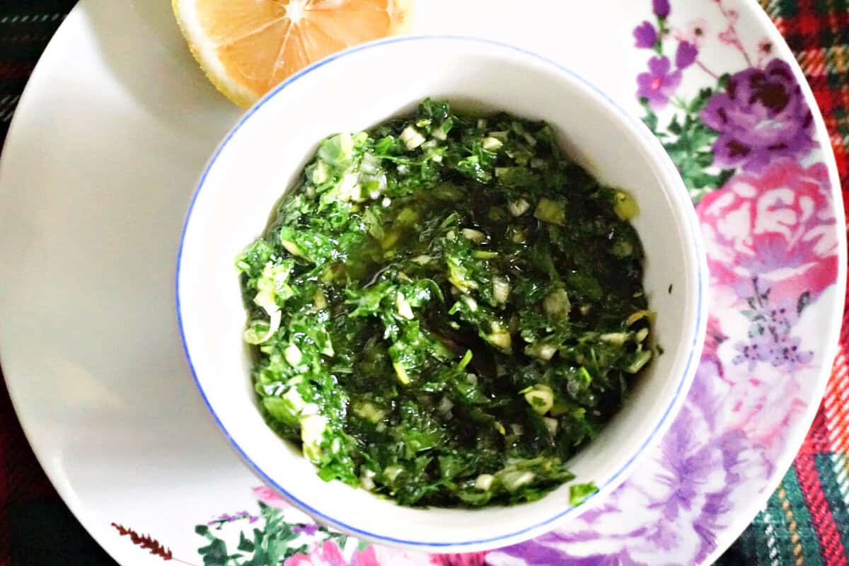 A white ramekin with parsley sauce with half a lemon next to it.