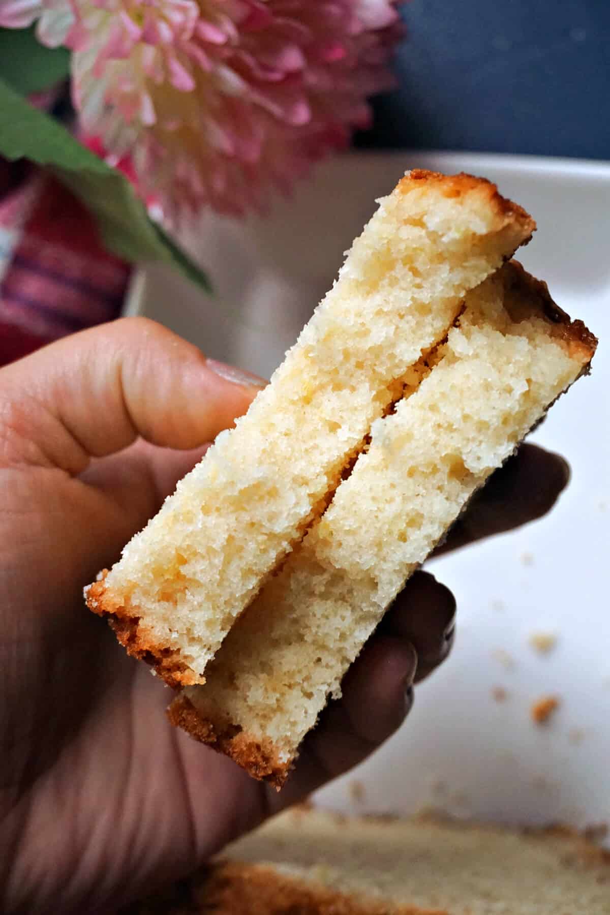 A hand holding 2 halves of a slice of cake.